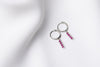 A pair of silver hoop earrings with a dangle of pink cubic zirconias on a white fabric surface.