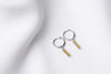 A pair of silver hoop earrings with a dangle of yellow cubic zirconias on a white fabric surface.