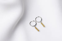A pair of silver hoop earrings with a dangle of yellow cubic zirconias on a white fabric surface.