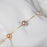 This gold chain bracelet featuring three different coloreed pearls on a white backgroung.