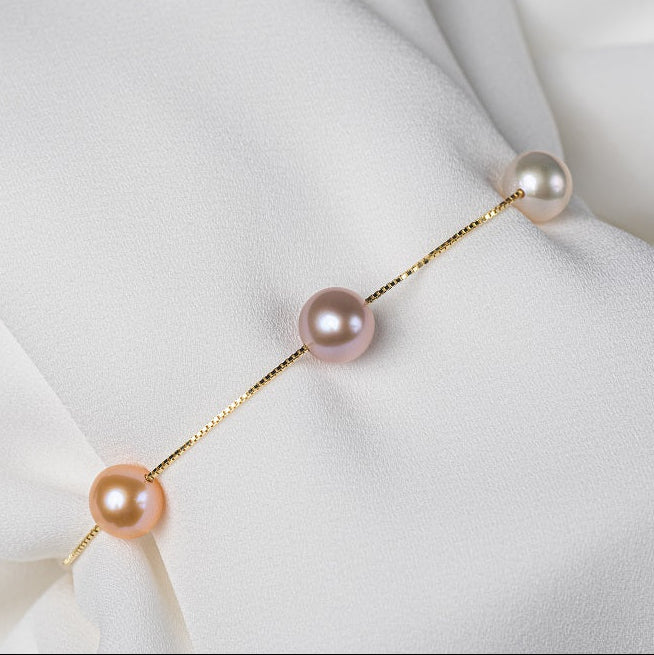 This gold chain bracelet featuring three different coloreed pearls on a white backgroung.