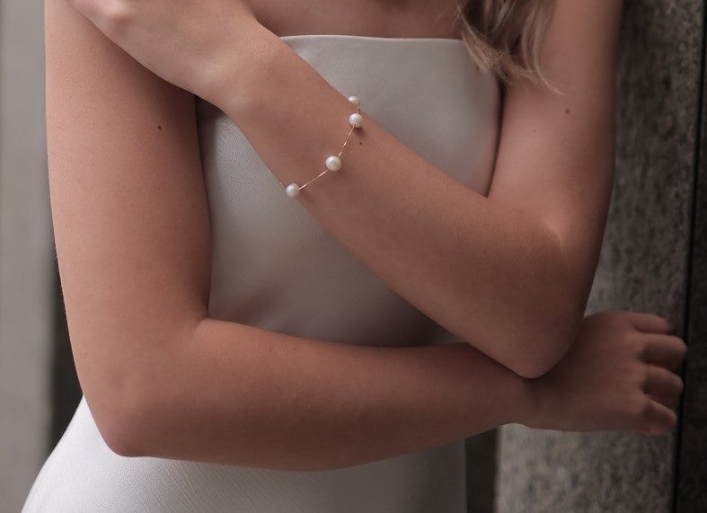 Model wearing a thin chain bracelet with white pearls.