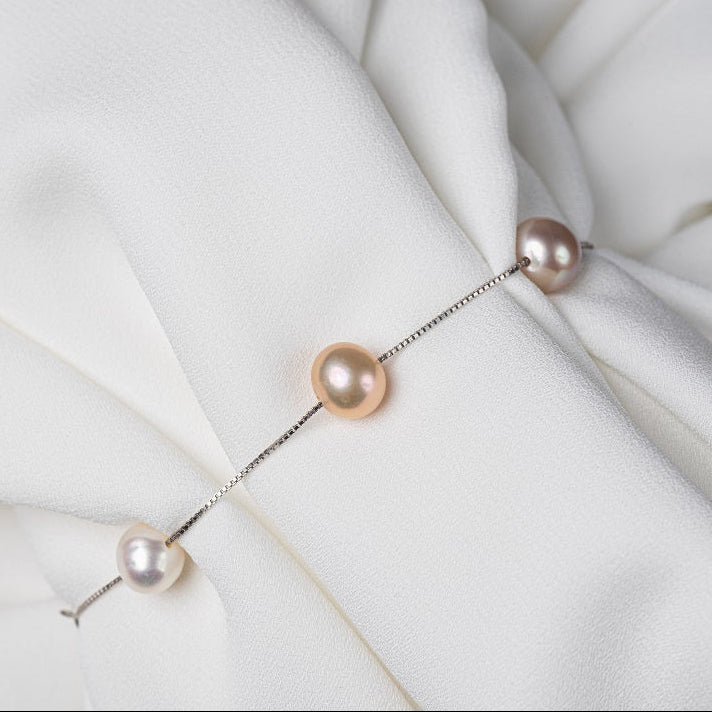 I thin silver chain braclet feayturing a mixture of coloured pearls on a white clocth background.