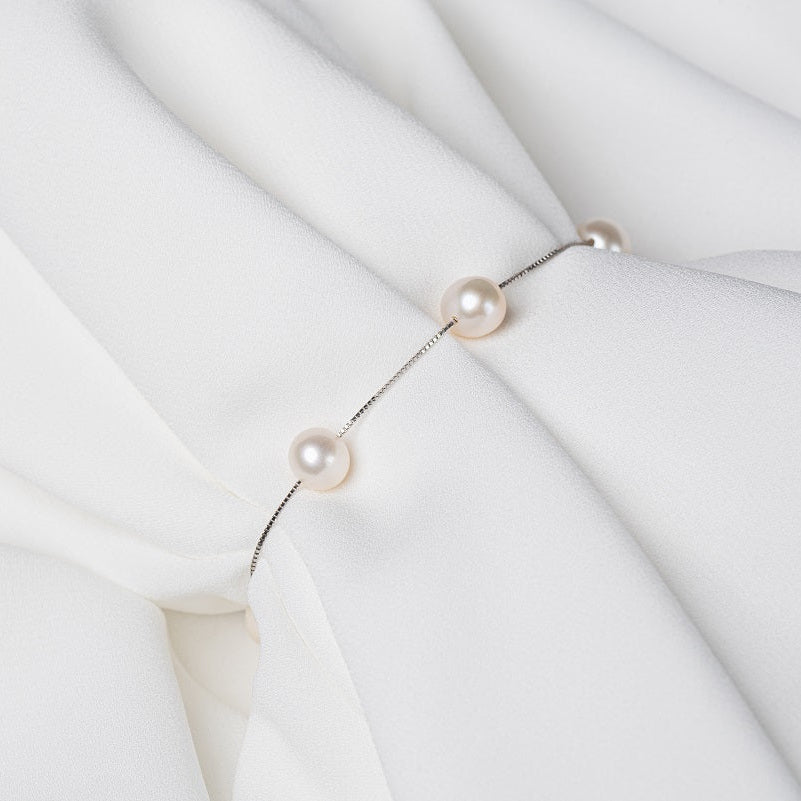 Fine chain bracelet featuring white pearls on a white cloth background
