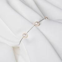Fine chain bracelet featuring white pearls on a white cloth background