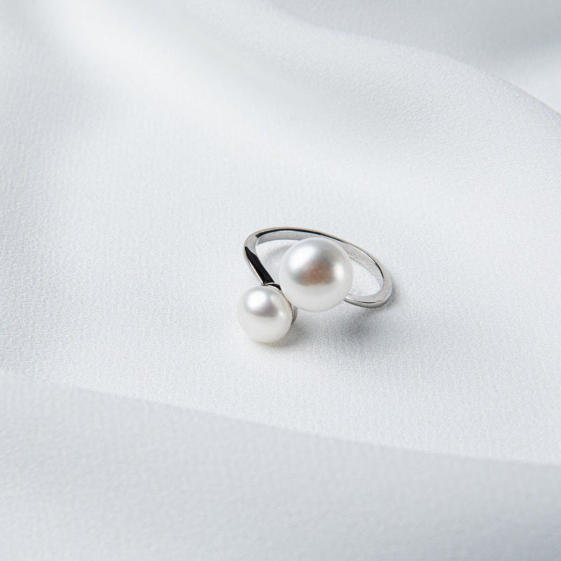 An adjustable silver ring with two white button-shaped pearls placed on a white fabric surface.
