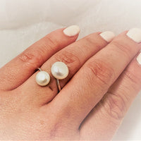 Close up of a womans hand wearing a thin silver ring featuring two white pearls.