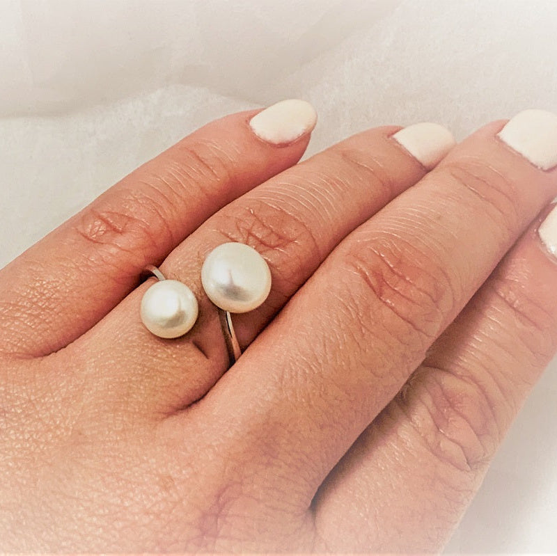 Close up of a womans hand wearing a thin silver ring featuring two white pearls.