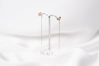 A pair of dangle earrings with a drop tail, butterfly backs, and a silver-colored post on a white stand against a white backdrop.