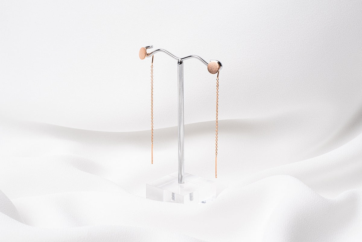 A pair of dangle earrings with a drop tail, butterfly backs, and a silver-colored post on a white stand against a white backdrop.