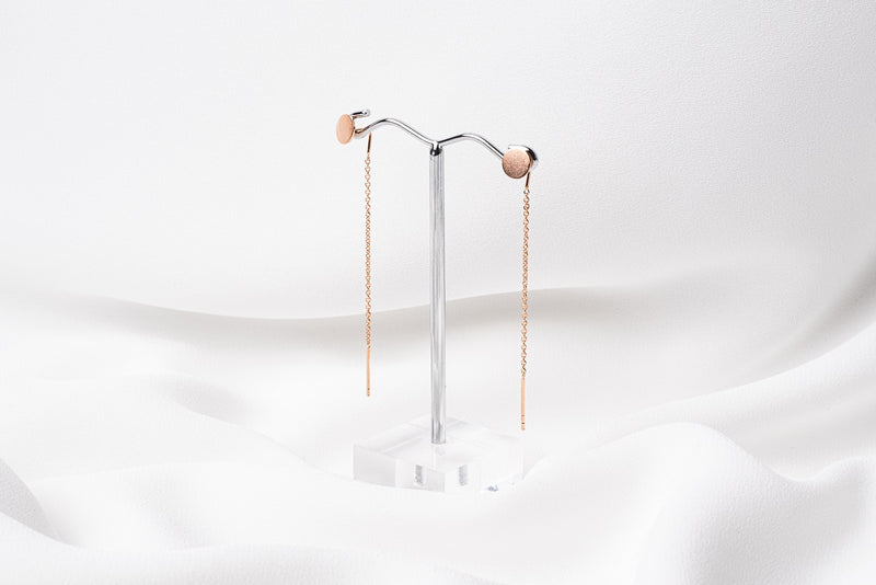 A pair of dangle earrings with a drop tail, butterfly backs, and a silver-colored post on a white stand against a white backdrop.