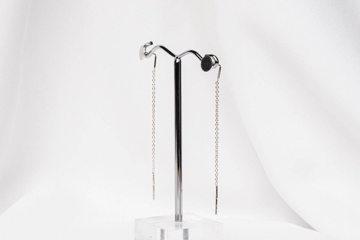 A pair of dangle earrings with a drop tail, butterfly backs, and a silver-colored post on a white stand against a white backdrop.