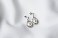A pair of silver Encanto pearl earrings displayed on a white background.