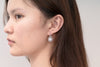 A pair of silver Encanto pearl earrings displayed on an asian woman model.