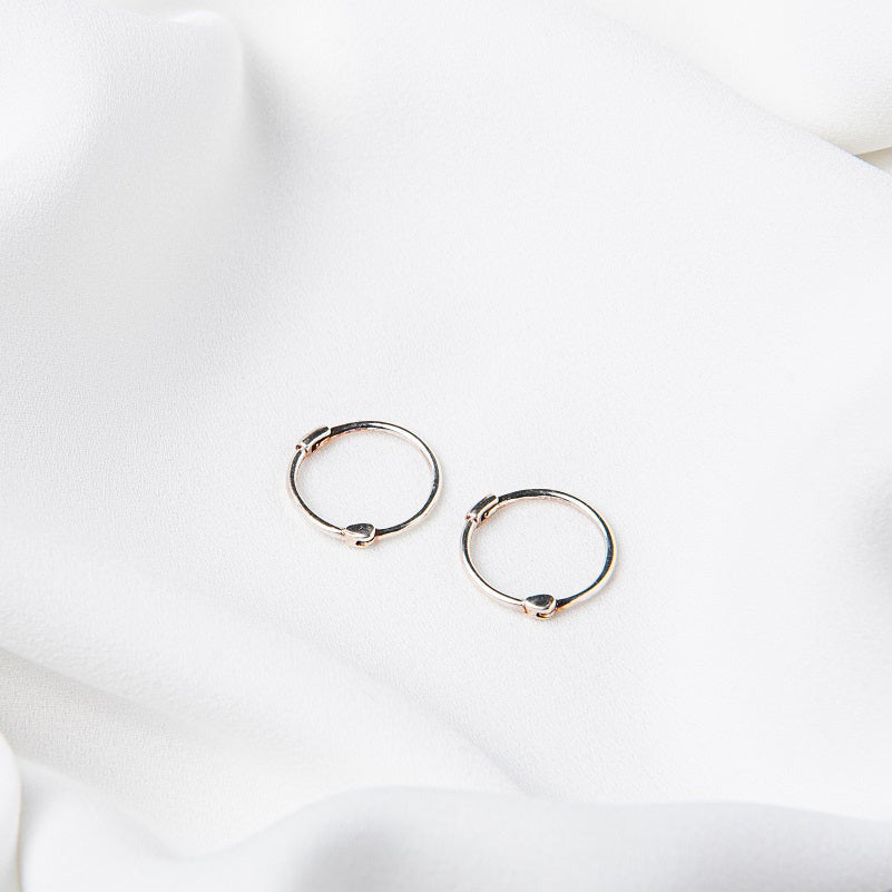 Two small silver hoop earrings placed on a white surface.
