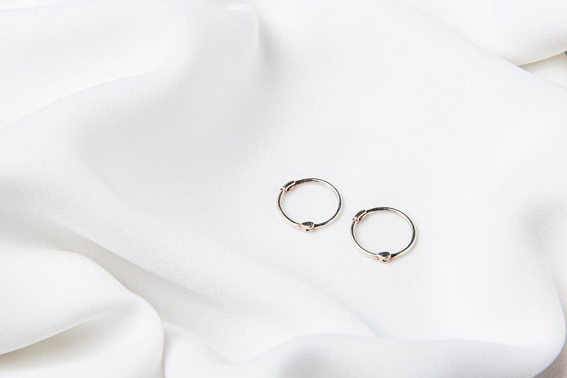 Two small silver hoop earrings placed on a white surface.