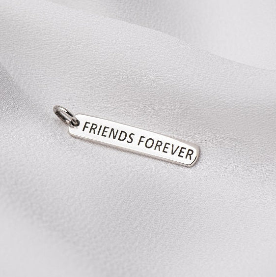 A silver pendant with the inscription 'Friends Forever' displayed on a white fabric surface.