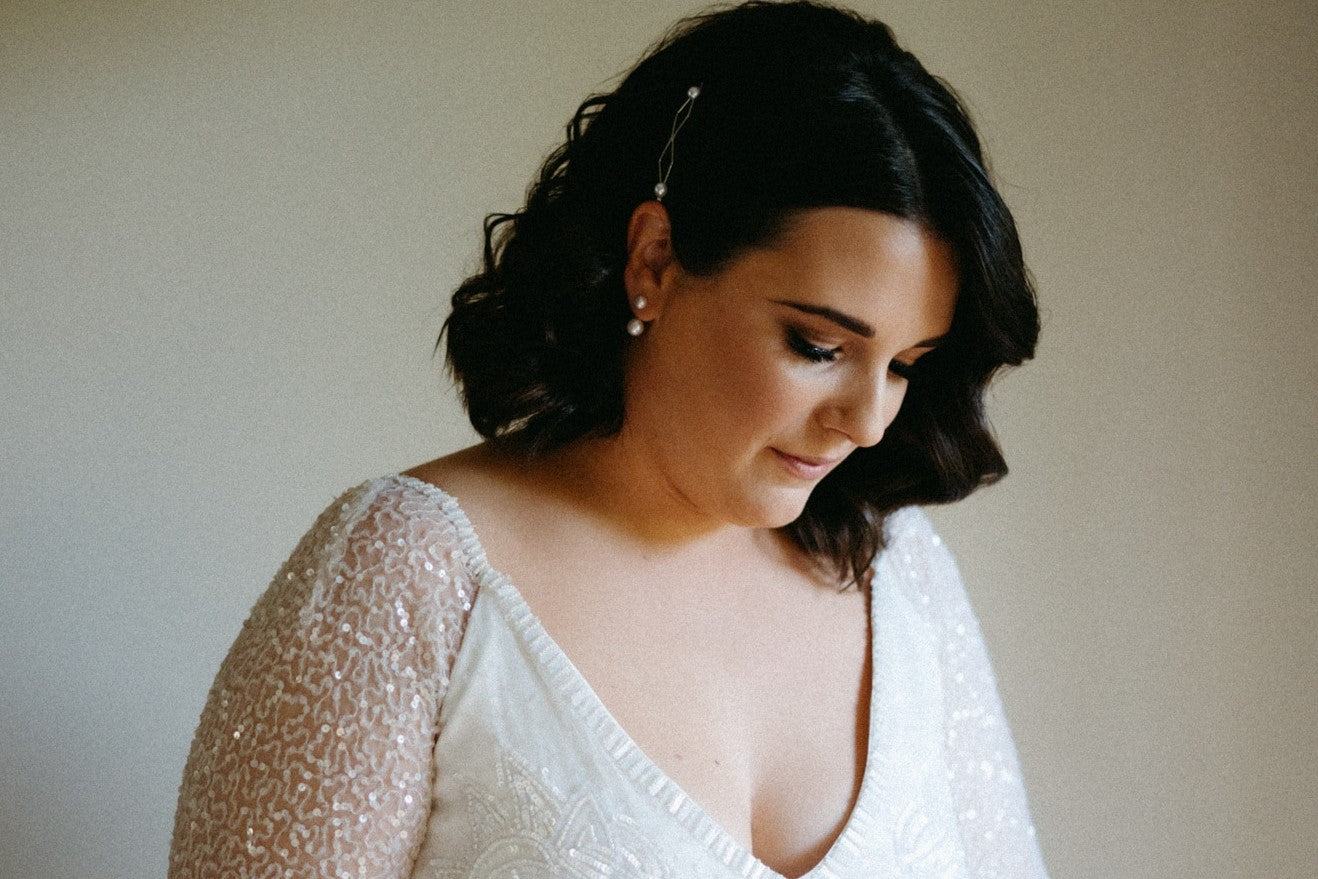 A pair of pearl stud earrings displayed on a female model in a bridal dress.