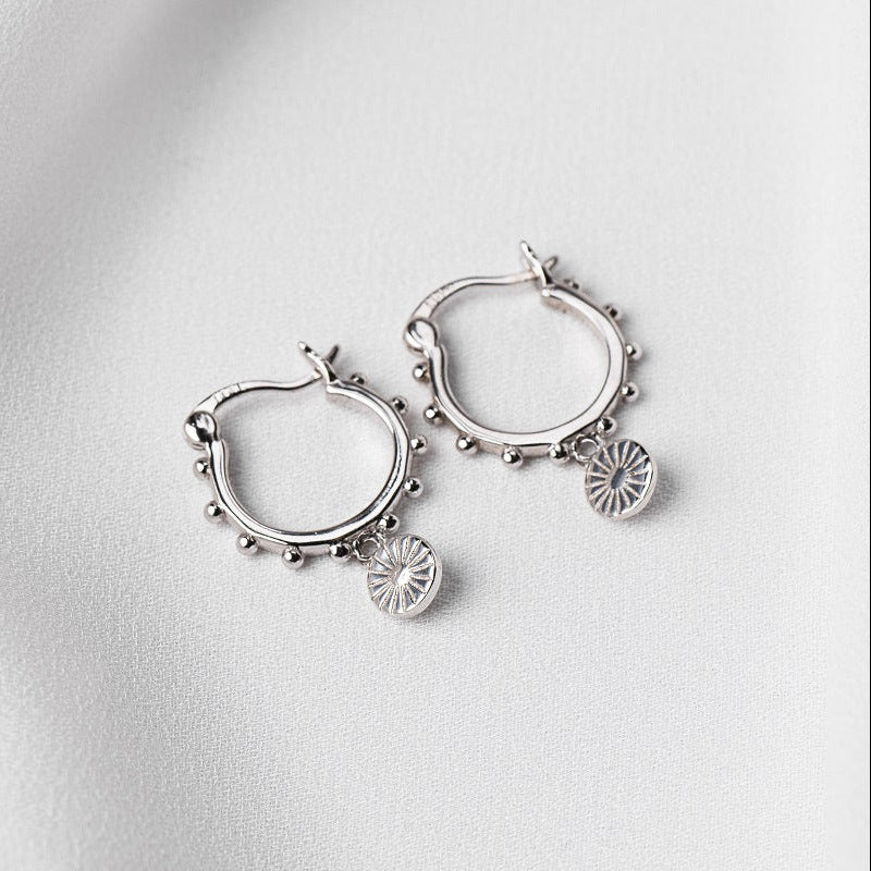 A pair of sterling silver hoop earrings with dangling good luck charms on a white fabric surface.