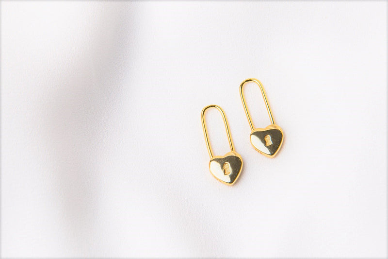 A pair of gold heart lock shaped earrings on a white background