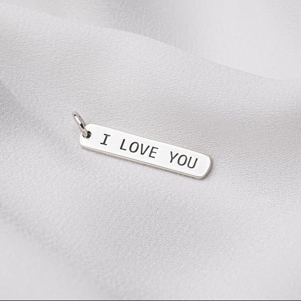 Silver pendant with "I love you" engraved on it. On a white cloth background