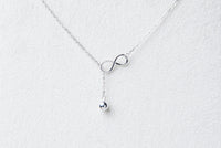 Fine chain drop style necklace with infinity pendant on a white background
