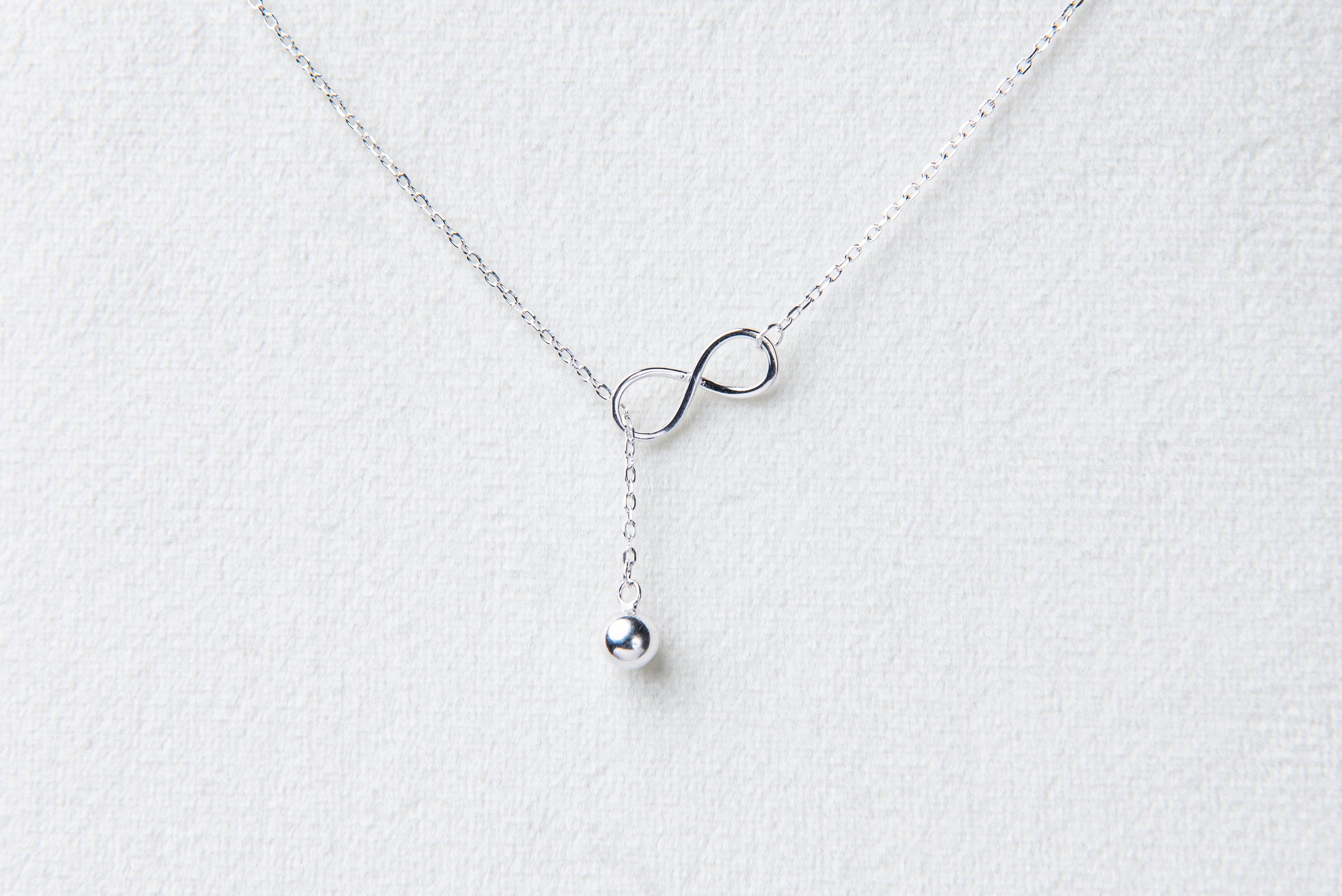 Fine chain drop style necklace with infinity pendant on a white background