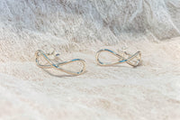 Infinity shaped silver stud earrings on a textured white background