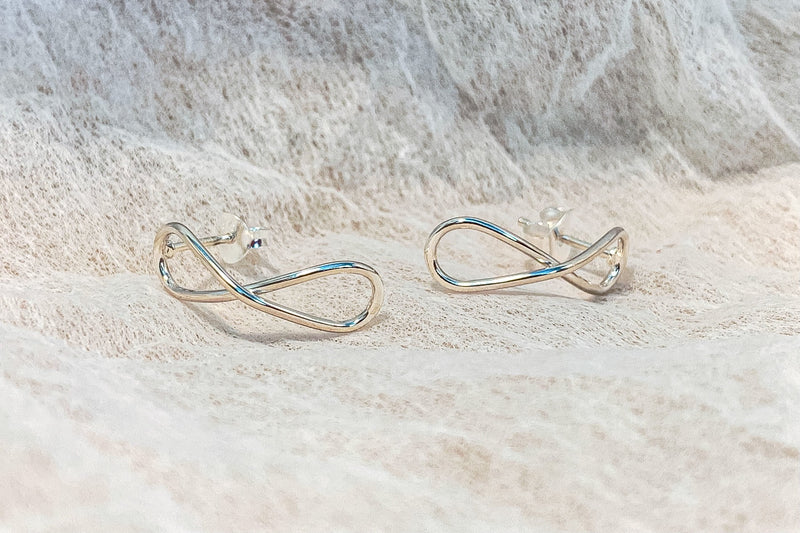 Infinity shaped silver stud earrings on a textured white background