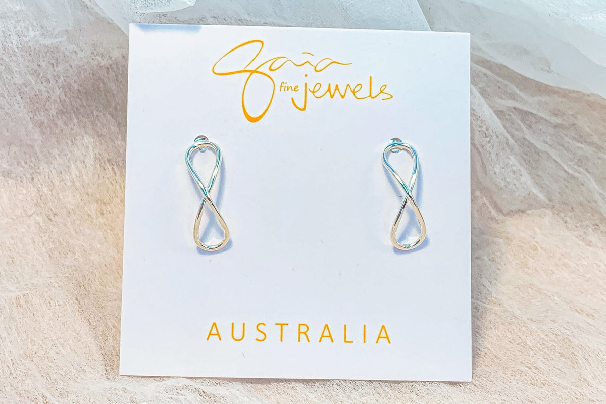 Infinity shaped silver stud earrings on a white display card with a textured white background
