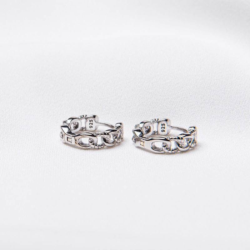 A pair of interlinked silver hoop earrings on a white background, showcasing a patterned design.