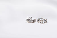 A pair of interlinked silver hoop earrings on a white background, showcasing a patterned design.