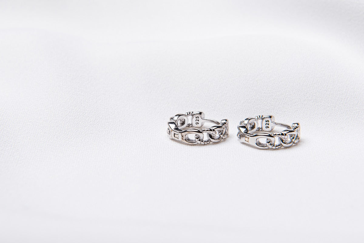 A pair of interlinked silver hoop earrings on a white background, showcasing a patterned design.