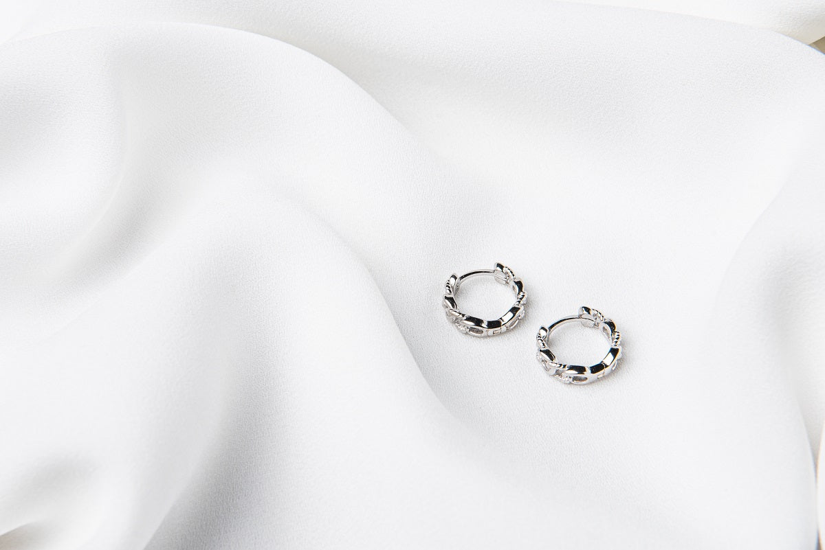 A pair of interlinked silver hoop earrings on a white background, showcasing a patterned design.