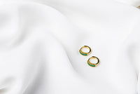 A pair of gold vermeil earrings with green cubic zirconias on a white cloth background