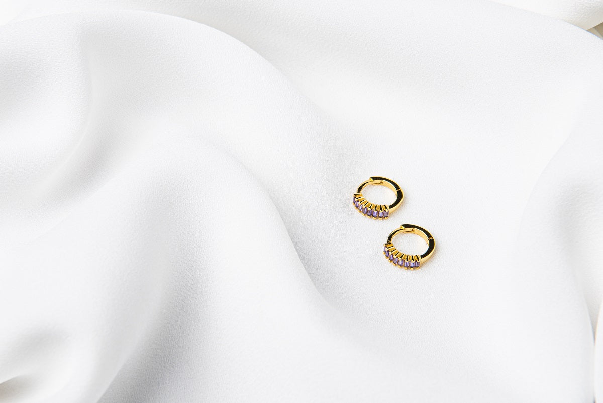 A pair of gold vermeil earrings with purple cubic zirconias on a white cloth background