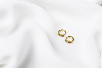 A pair of gold vermeil earrings with rainbow cubic zirconias on a white cloth background