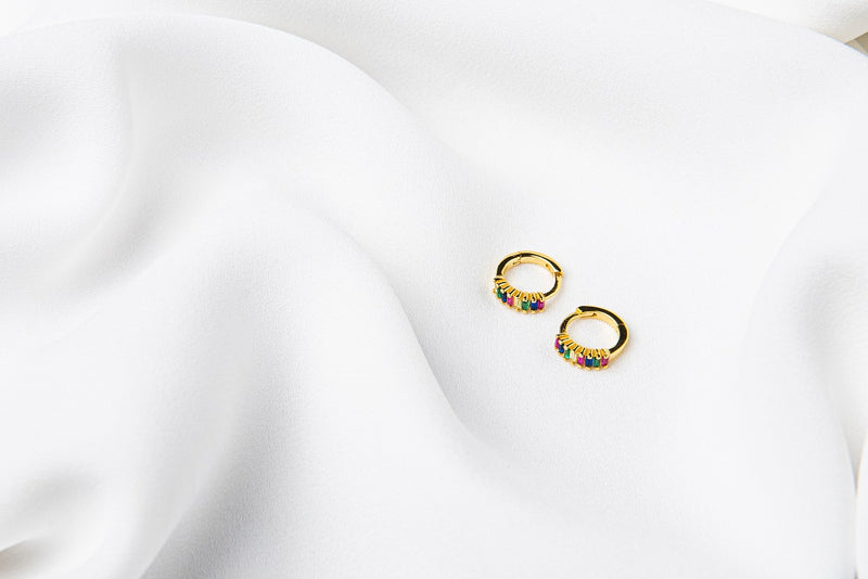 A pair of gold vermeil earrings with rainbow cubic zirconias on a white cloth background