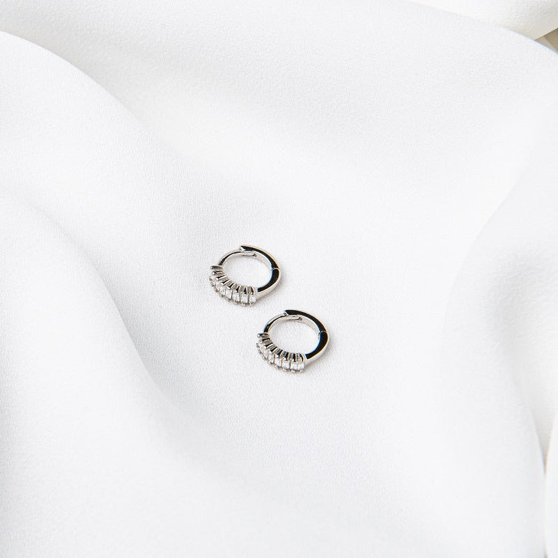 A pair of silver earrings with cubic zirconias on a white cloth background