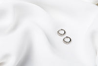 A pair of silver earrings with cubic zirconias on a white cloth background