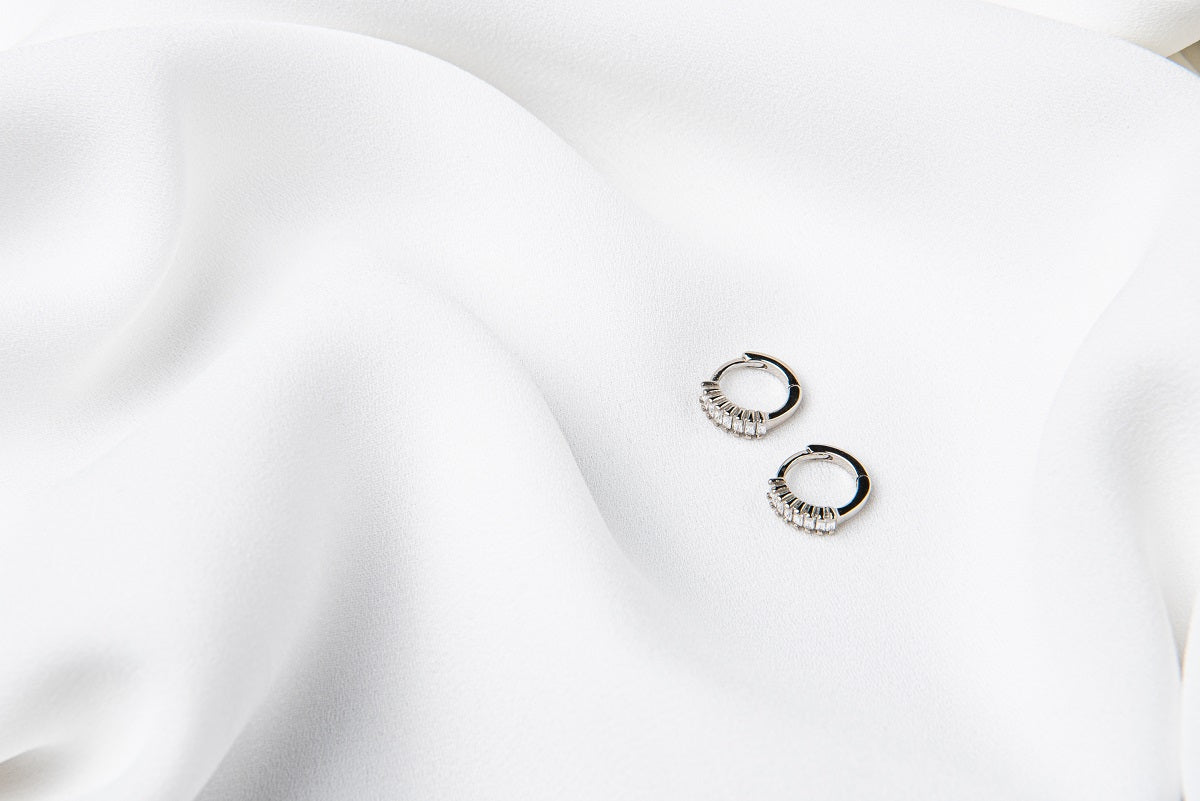 A pair of silver earrings with cubic zirconias on a white cloth background