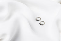 A pair of silver earrings with black cubic zirconias on a white cloth background