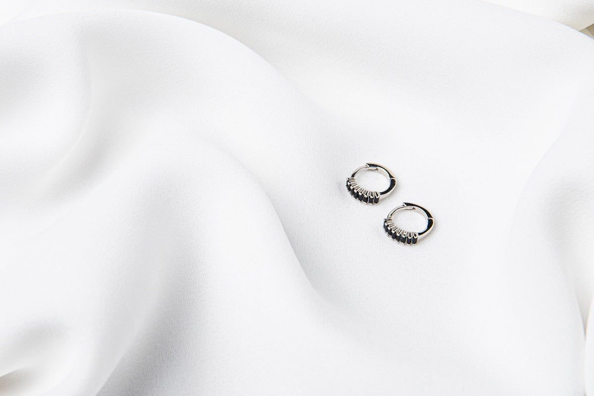 A pair of silver earrings with black cubic zirconias on a white cloth background
