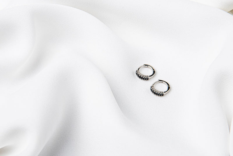 A pair of silver earrings with black cubic zirconias on a white cloth background