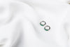 A pair of silver earrings with green cubic zirconias on a white cloth background