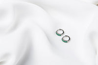 A pair of silver earrings with green cubic zirconias on a white cloth background