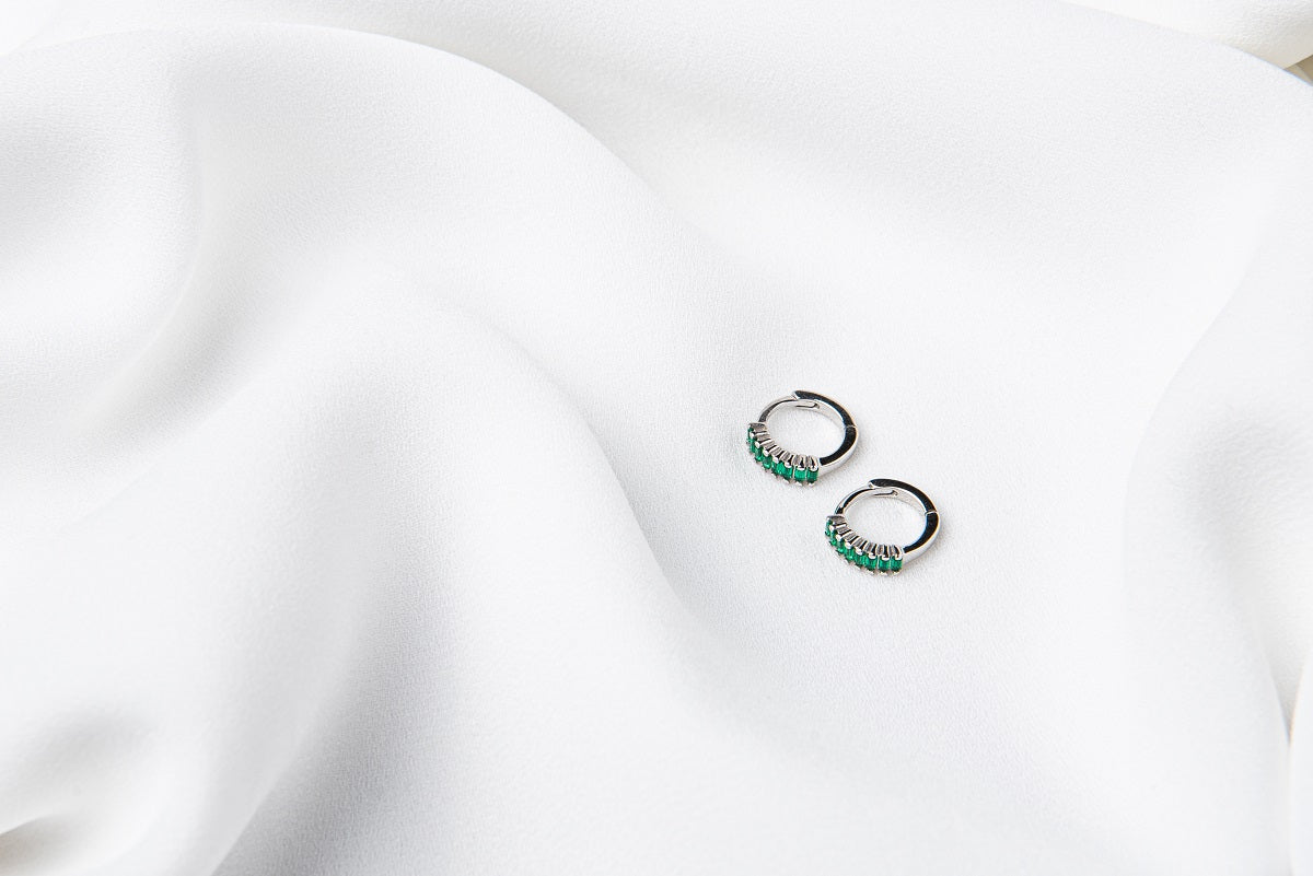 A pair of silver earrings with green cubic zirconias on a white cloth background