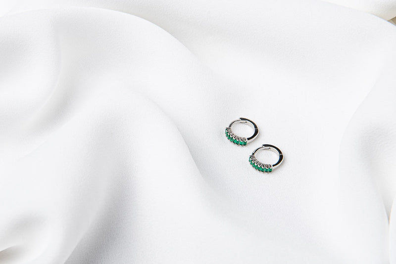 A pair of silver earrings with green cubic zirconias on a white cloth background