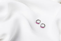 A pair of silver earrings with purple cubic zirconias on a white cloth background