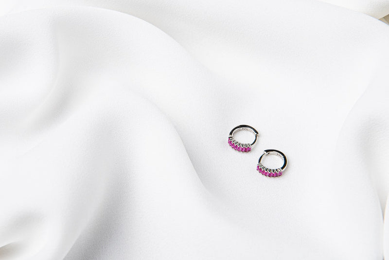 A pair of silver earrings with purple cubic zirconias on a white cloth background